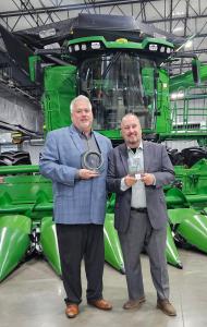 Len Anhold & Scott Hoffman hold John Deere Sustainability Award for Fisher Barton in front of a green combine