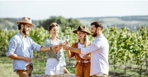 Two couples toasting with wine glasses at a vineyard table surrounded by grapevines, representing the lifestyle available to homeowners at La Brisa Toscana near San Miguel de Allende.