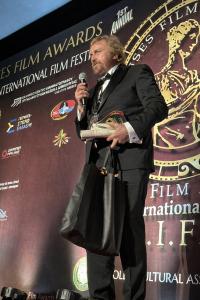 Alessandro Vantini stands on stage at Muses Film Awards and is presented with the Best Actor Award; his work has earned more than 161 international film awards