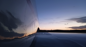 Close-up view of an aircraft fuselage reflecting a sunset sky with soft clouds and fading light.