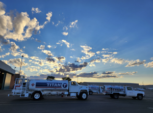 Several aviation fuel trucks lined up at an airport with dramatic clouds and sun rays in the sky.