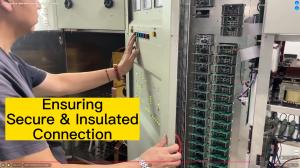 Man in black t-shirt with red bracelet pushes a color button on the control panel of an AM transmitter. Right side is a rack with stacked PCB power modules featuring many green LEDs. Large yellow text box says, "Ensuring Secure & Insulated Connection."