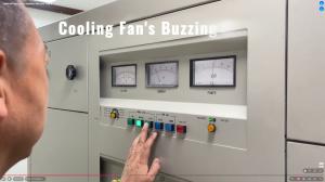 Profile view of a man pressing a green button on a large beige transmitter control panel. The panel features three analog meters, various indicator lights, and text overlay reading "Cooling Fan's Buzzing."