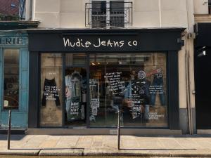 Façade du store Nudie Jeans dans le Marais à Paris, avec vitrines illustrées et entrée centrale, située au 19 Rue du Pont aux Choux.