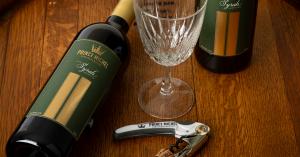 Prince Michel Syrah wine bottle, wine glass, and corkscrew arranged on a wooden surface