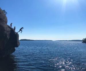 Three young swimmers jump from a steep, high cliff into a lake.
