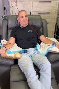 Dr. Kevin Greene receiving EBOO therapy at Confidia Health Institute in Bristol, Connecticut, with medical tubing connected to a blood filtration and oxygenation machine in the background.