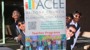 Group of students in suits and sunglasses playfully peeking from behind an ACEE Arizona Council on Economic Education sign promoting teacher programs.