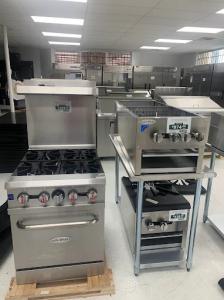 A clean, well-lit HorecaStore showroom interior displaying stainless steel commercial kitchen equipment, including gas ranges, ovens, and prep units arranged neatly for restaurant buyers.