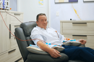 Man receiving EBOO therapy while seated in a recliner at Confidia Health Institute with tubing connected to a filtration system.