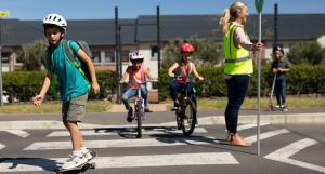 image of chidren riding and walking across the street as a crossing guard holds sign to stop traffic