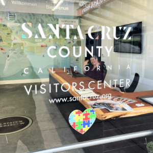 Glass door of Santa Cruz County Visitors Center with a person inside and a colorful puzzle heart decal