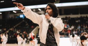 Ashwin Gane performing on court during an NBA G League halftime show, pointing toward the audience while holding a microphone.