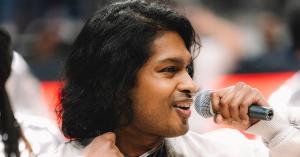 Side profile close-up of Ashwin Gane performing with a microphone during a live basketball game halftime show.