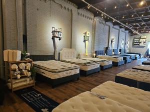Interior of a SleePare mattress showroom with multiple mattresses on display, including Avocado and MLILY beds, in a renovated brick building with industrial-style lighting.