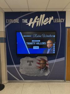 Wall-mounted interactive display at Trinity High School beneath “Explore the Hiller Legacy” graphic, showcasing a searchable digital archive of yearbooks, records, and alumni content.