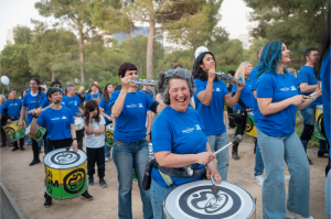 a group of musicians in blue t-shirts play as they lead a group through a park