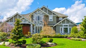 The front exterior of a large stone-accented home with a perfectly manicured lawn, ornamental trees, and clean garden borders.