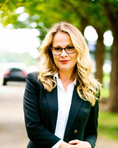 Portrait of Eleni Kapetanios, psychotherapist, standing outdoors in Guelph, Ontario. wearing glasses and a black blazer in a natural setting