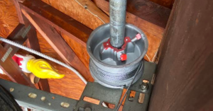 Close-up of a repair technician's hands carefully adjusting the electronic safety photo-eye sensor at the base of a garage door track.