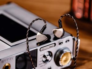 Kiwi Ears Halcyon tribrid in-ear monitors with USound MEMS speaker technology resting on a desktop audio device with braided cable and metal housing.