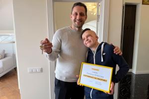 Roman Oleksiv, who survived the 2022 shelling of Vinnytsia, stands with his father in their new apartment, smiling.