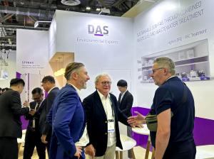 DAS Environmental Experts' booth at a trade show: Several men in business attire are talking in front of a white booth featuring branding and information on sustainable exhaust gas and wastewater treatment in the semiconductor industry.