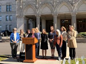 A group of 10 women at a press conference, standing behind a lectern, outside and in front of the Connecticut State Capitol, Hartford, CT, held in support of passing Senate Bill 259