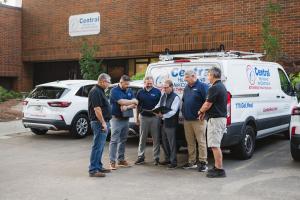 Team of HVAC technicians from Central Heating and Air Conditioning discussing service plan near branded van outside office building
