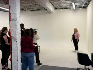 VIP Ignite Certified Production Assistant Program participants operate a professional video camera during a live studio production session, with a female talent posed against a white seamless backdrop as trainees gain hands-on behind-the-scenes production