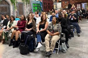 A diverse crowd of aspiring models and actors seated in rows inside a spacious Hollywood production studio with exposed wooden beam ceilings and film set backdrops, attending a VIP Ignite live industry event as part of the organization's 20-year history o