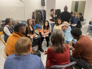 A diverse group of aspiring models and actors seated in a circle engage in an intimate one-on-one networking session with a working entertainment industry professional at a VIP Ignite New York event, reviewing portfolios and exchanging career guidance whi