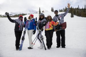 Group of Black skiers and snowboarders smiling and posing with skis and snowboards on a snowy mountain slope.