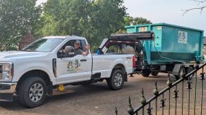 Trash Pandy owner waving from branded delivery truck hauling teal dumpster in Smyrna Tennessee