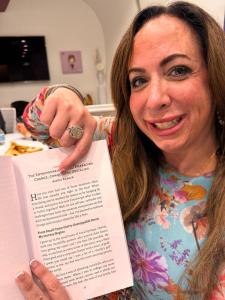 Alycia Kaback, Co-Founder of VIP Ignite, smiles and holds up her co-authored chapter titled "The Entrepreneurial Journey: Embracing Change, Conquering Obstacles" from a published book alongside Kevin Harrington of Shark Tank fame, showcasing her entrepren