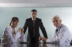 photo of a health care manager in a business suit standing at a conference table with two health care professionals in uniforms sitting at the table