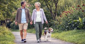 Older couple walking dog on park path — balance and mobility for active aging