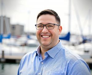 Headshot of Mike Clapper, smiling in a blue shirt with a marina in the background