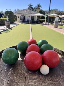 Red and green bocce balls with a white pallino on a wooden rack beside a manicured bocce court at The Club at Mediterra.