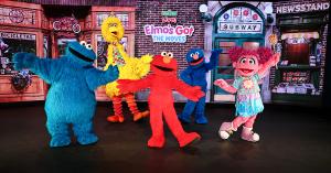 Colorful Sesame Street characters Cookie Monster, Big Bird, Elmo, Grover, and Abby Cadabby cheerfully dance on stage under a sign reading "Elmo's Got the Moves."