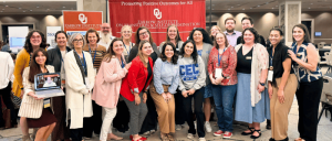 Group photo of diverse adults standing in front of a red Zarrow Institute banner at an indoor event promoting positive outcomes.