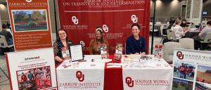 Three people sit behind a University of Oklahoma Zarrow Institute and Sooner Works informational booth at an indoor event.