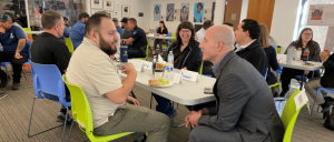 People engaged in lively conversation around tables in a bright, casual meeting or workshop setting.
