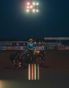 A cowgirl competes in pole bending at night