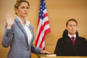 photo of a court room with a judge seated and a witness standing taking an oath to testify