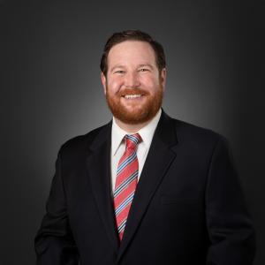 Headshot of John Kidwell, M.D. smiling and wearing a black suit and white shirt with a red and blue striped tie.