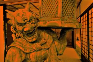 A statue of a demon holding a lantern in front of a Japanese interior