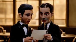 Film still from El día que me quieras: El Viaje de Gardel, showing two stylized stop-motion-inspired animated men in formal suits reading a paper together inside a warmly lit café.