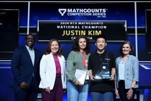 Justin smiles onstage with his trophy, his coach and representatives from MATHCOUNTS.