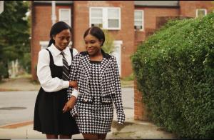 Two school girls walking along a street arm and arm; an official still image from the feature film FORTUITOUS premiering on VYRE Network beginning May 15, 2026